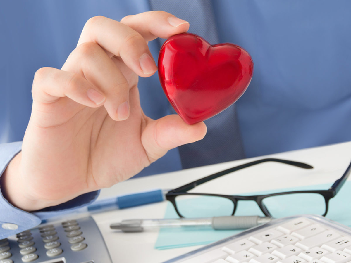 Hand holding a heart above a desk, keyboard and specticles
